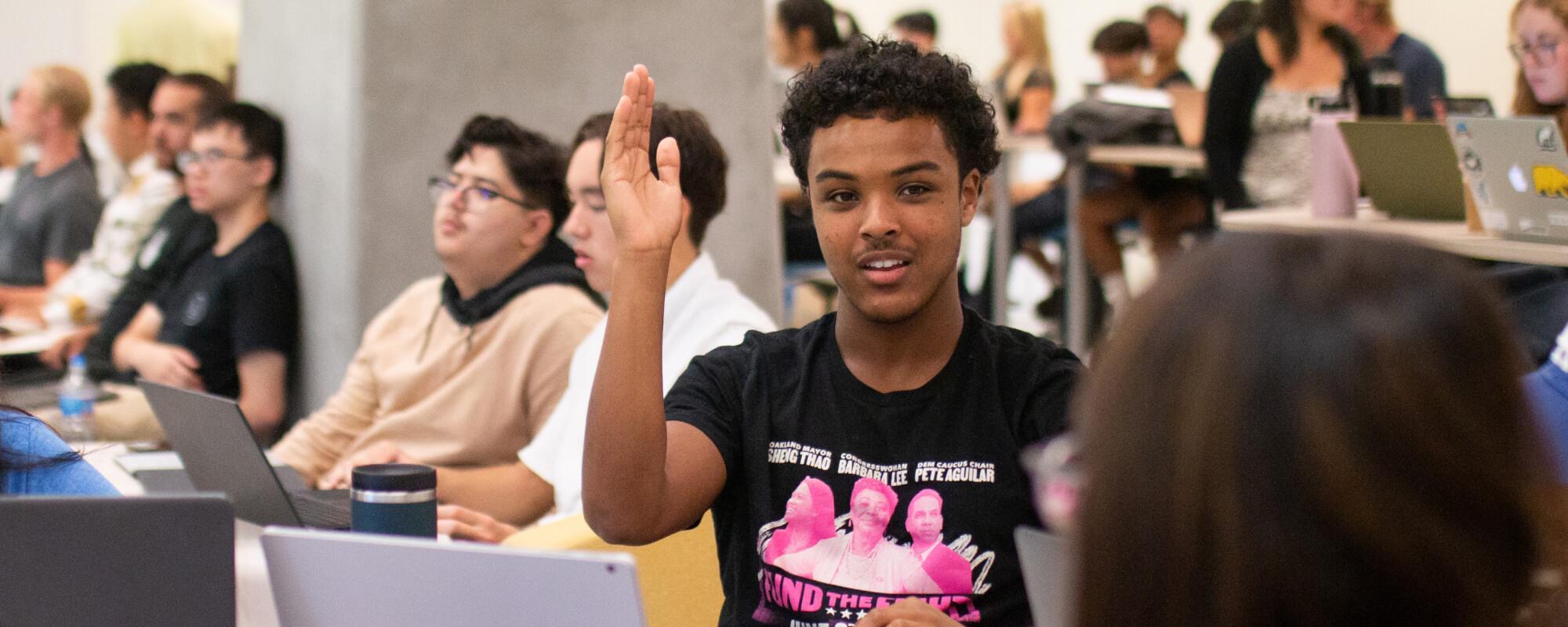 Student raising their hand in a classroom full of students